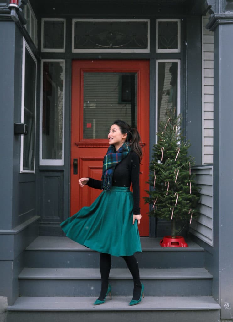 jean wang's christmas outfit with green heels, green skirt, black sweater, and plaid scarf
