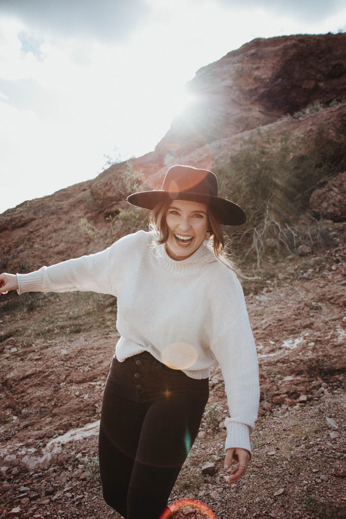 confident modest woman wearing black hat, loose white sweater, and black jeans