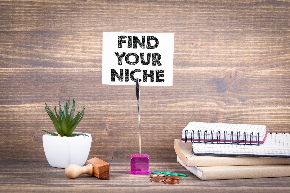 sign that says find your niche next to a little plant and some notebooks