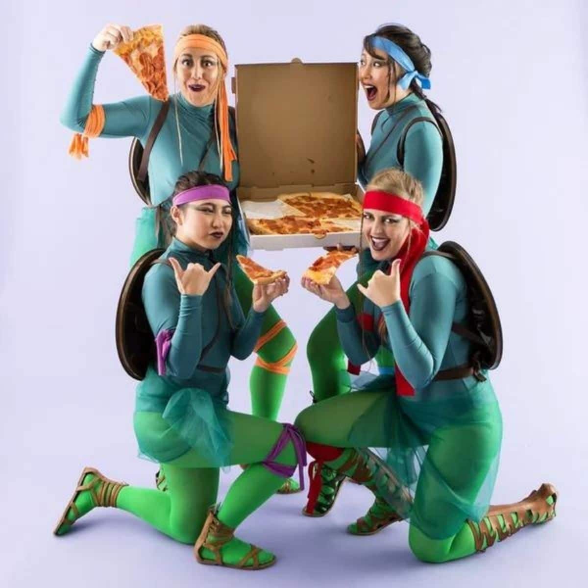 4 girls dressed up as the teenage mutant ninja turtles holding pizza