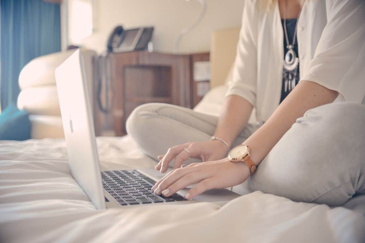 woman sitting on a bed typing on a laptop