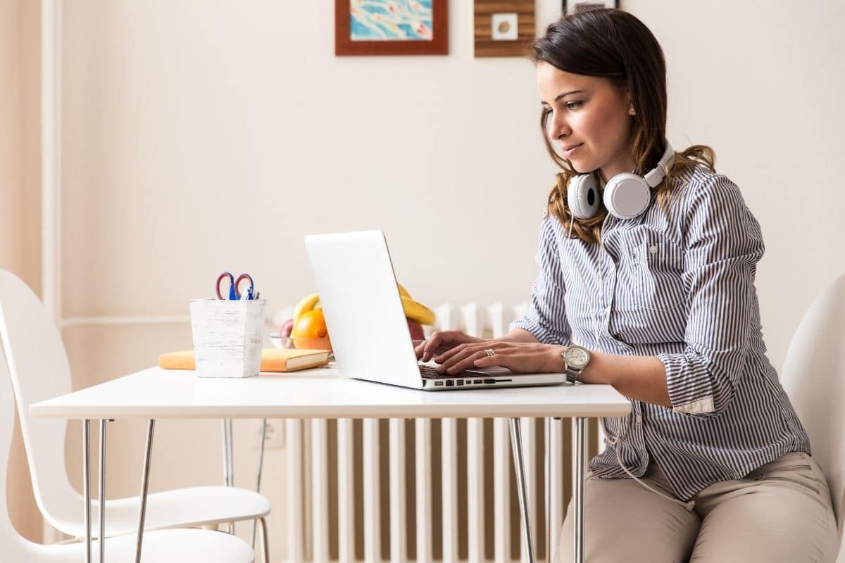a woman sitting down at a table blogging on her laptop