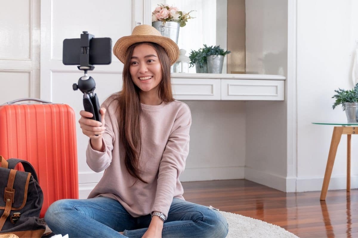 a woman sitting holding a camera and vlogging