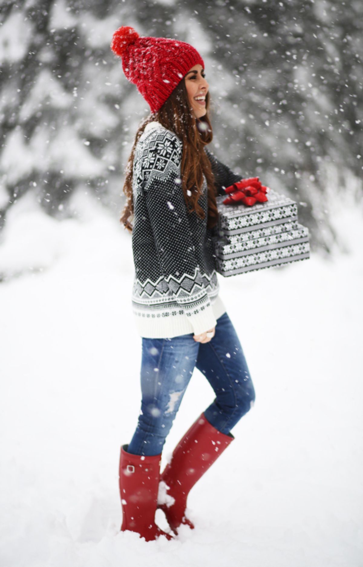 snowy day outfit with red beanie, christmas sweater, jeans, and red hunter boots