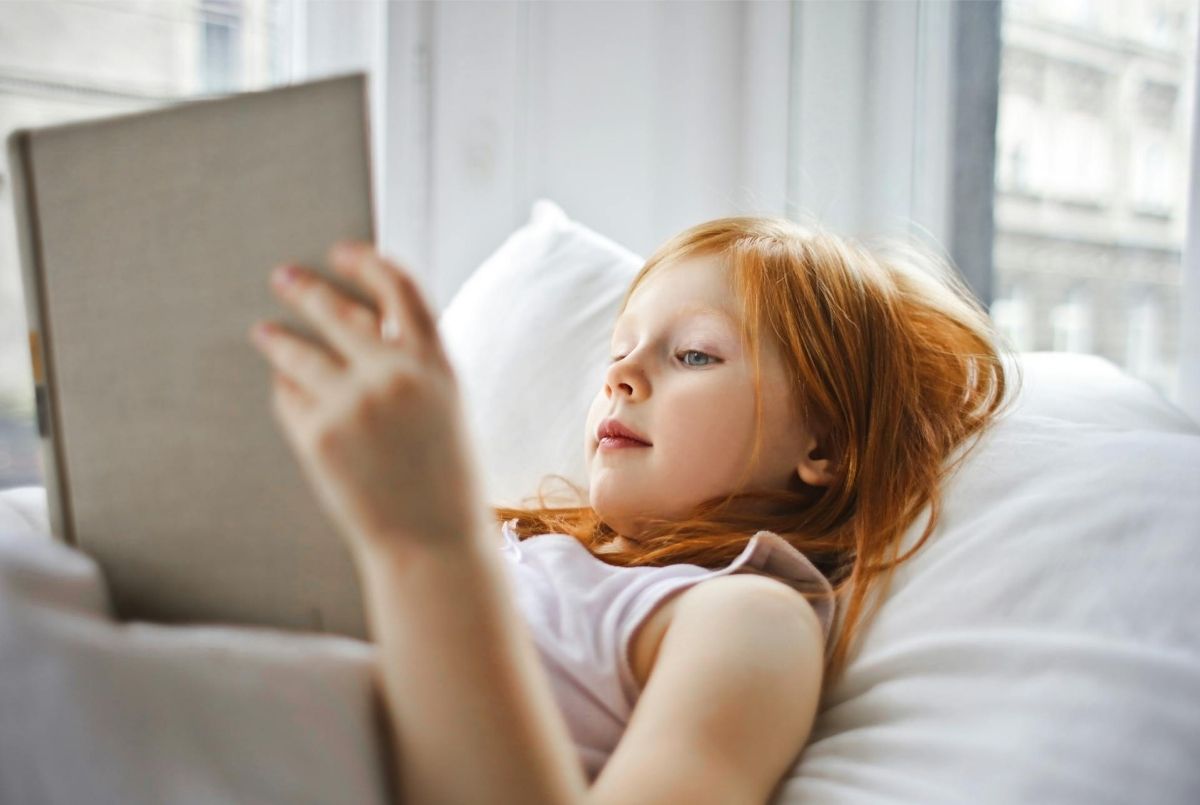 a girl reading a book while lying on bed