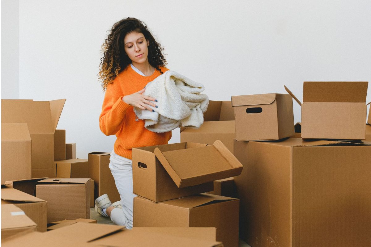 focused young relocating female packing belonging into cardboard boxes